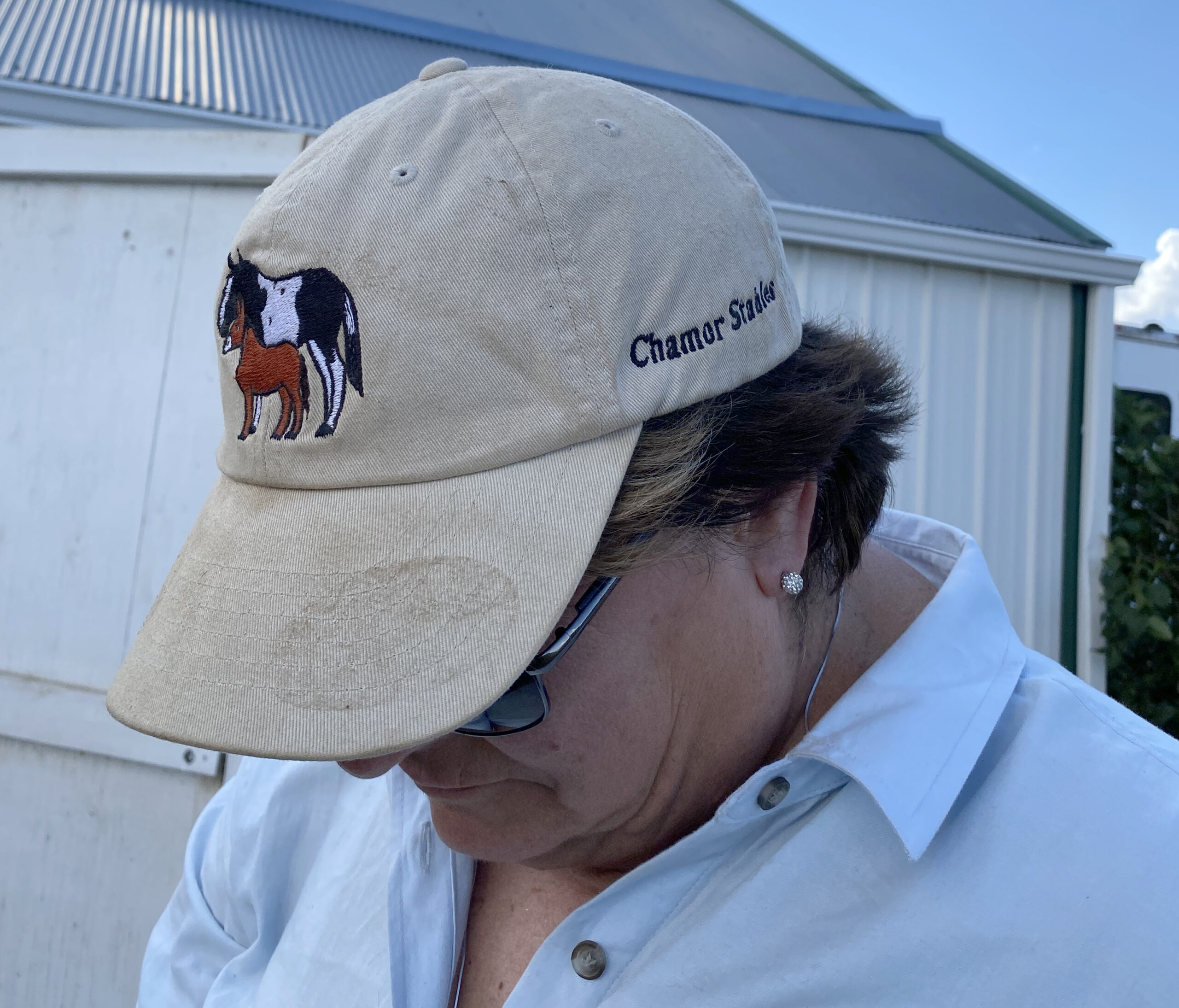 Female equine farmer shows her hat with a drawing of her horse and donkey.